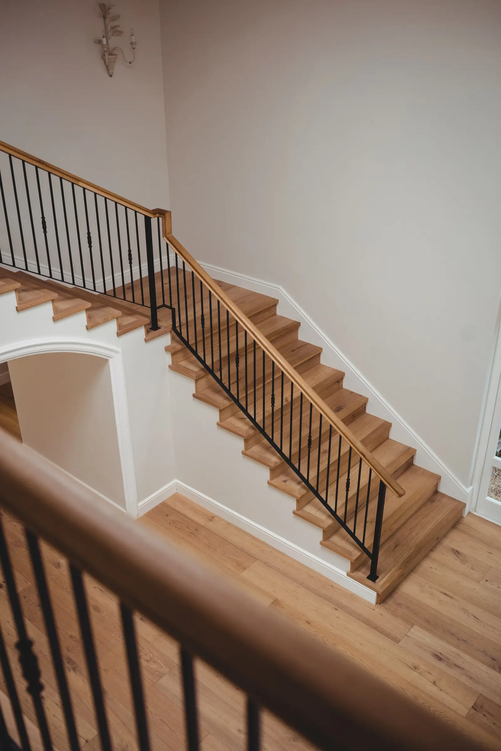 Dębowe schody z czarną balustradą przechodzące w drewnianą podłogę korytarza